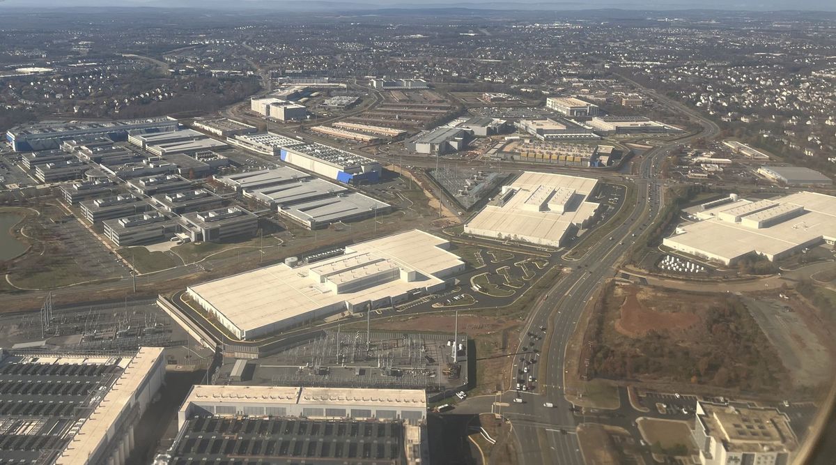 Luftaufnahme großer flacher Rechenzentrumshallen und Umspannwerke zwischen Straßen und Gewerbegebieten bei Ashburn, Virginia